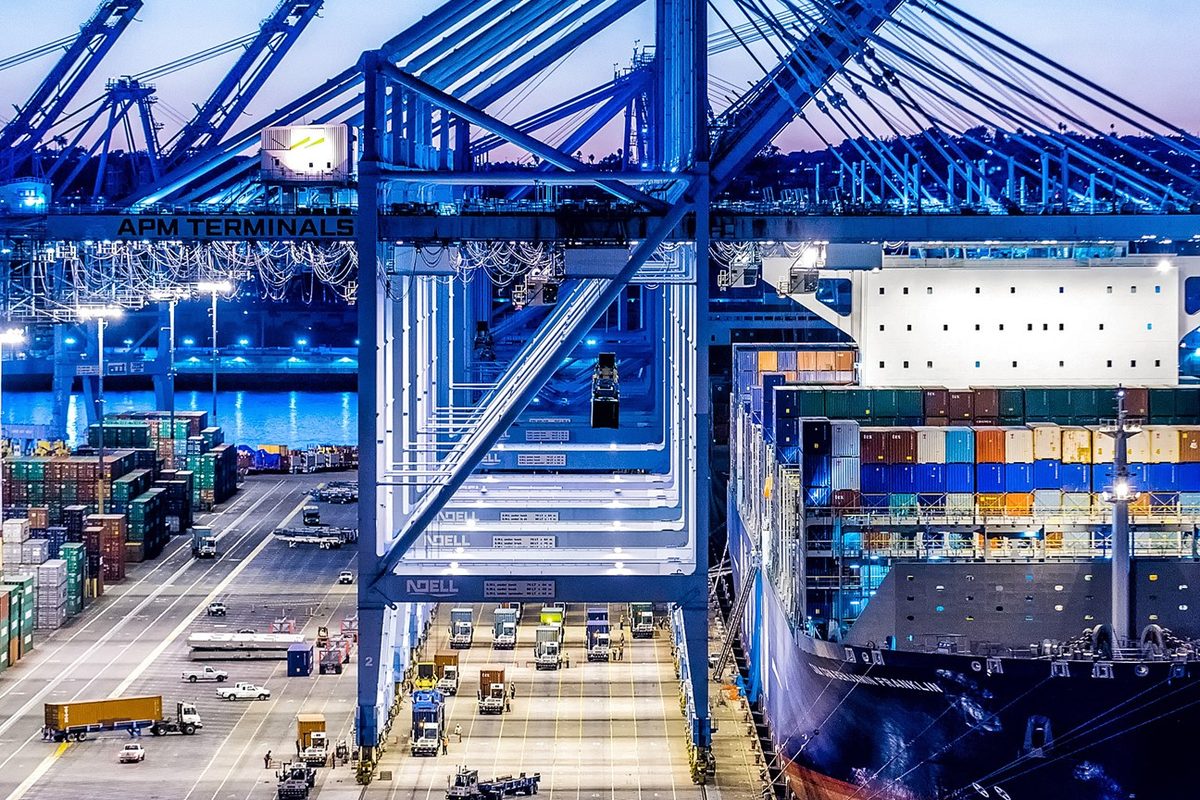 Container vessel alongside a floodlit terminal at dusk while gantry cranes work the stacks